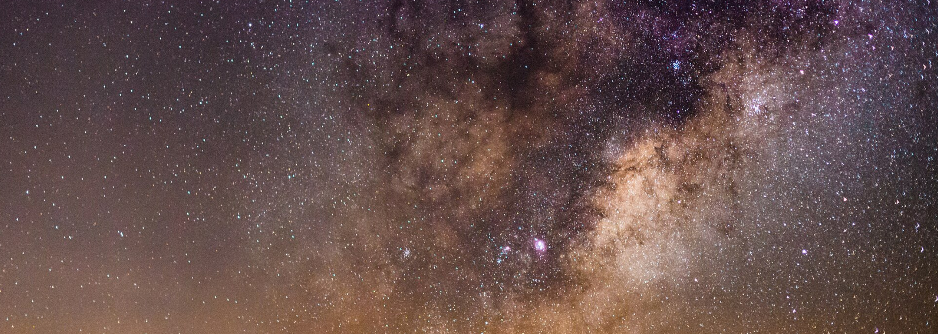 Night sky filled with stars, including the Milky Way galaxy. Brown, purple, and yellow hues.