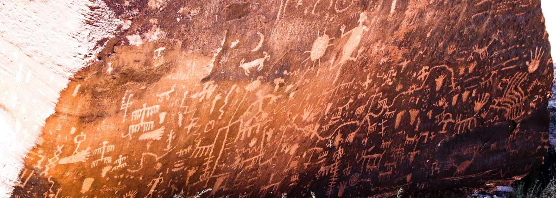 Petroglyphs carved into a reddish rock face. Figures of people and animals are visible.