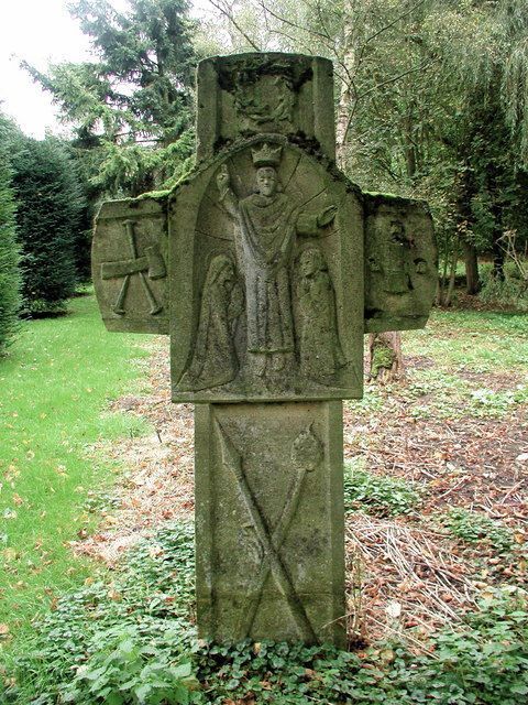 Stone cross with carved religious figures in a grassy outdoor setting.