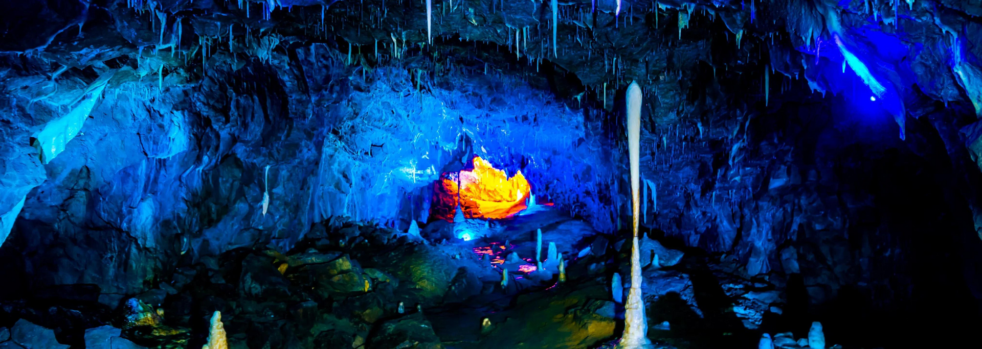 Blue cave with glowing orange formation at the center, illuminated by white stalactites.