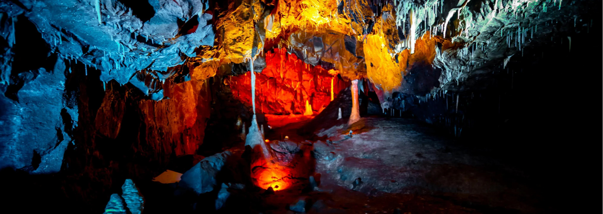 Cave interior lit with red and orange lights, highlighting stalactites and formations on the walls and floor.