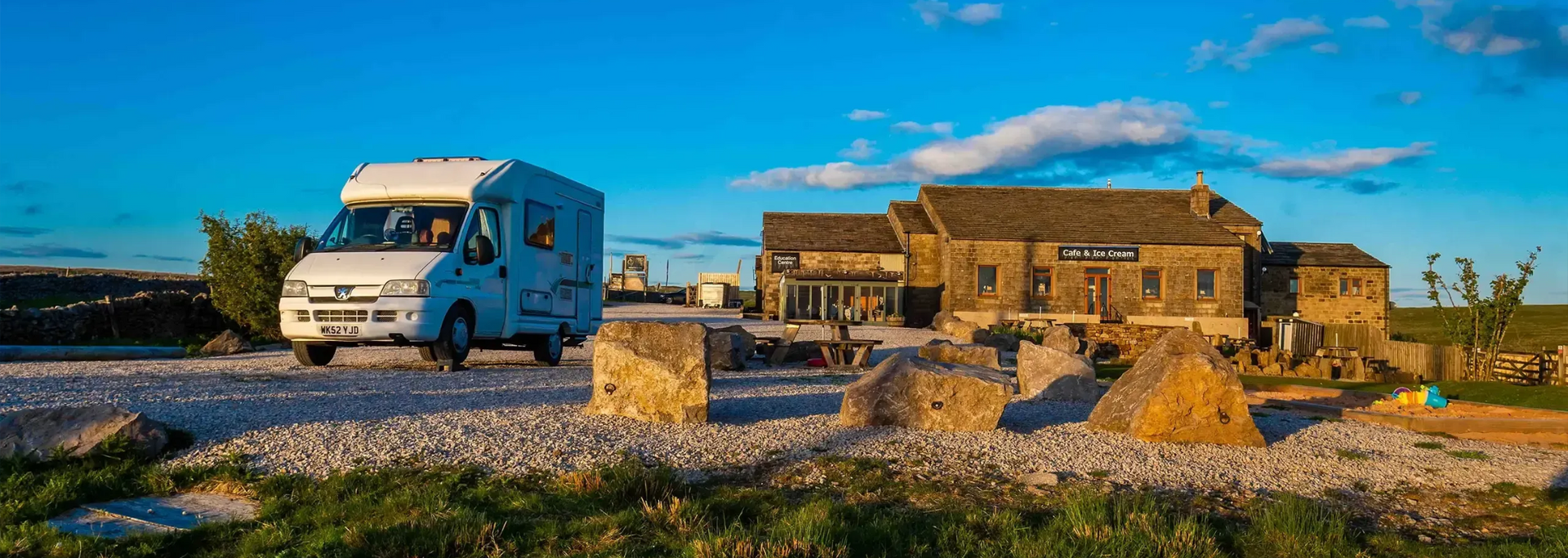 A white campervan parked in front of a stone building with a blue sky in the background.