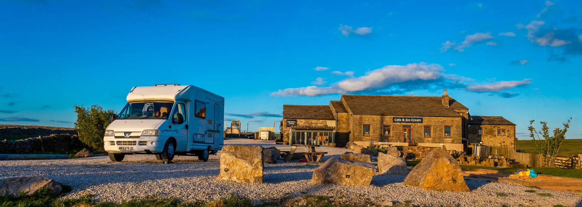 RV parked near a stone building under a blue sky, possibly a pub or inn.