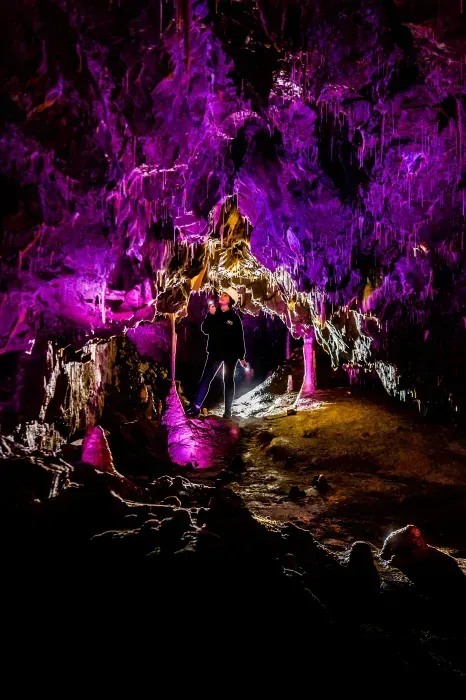 Person standing in a cave illuminated by vivid purple and gold lights