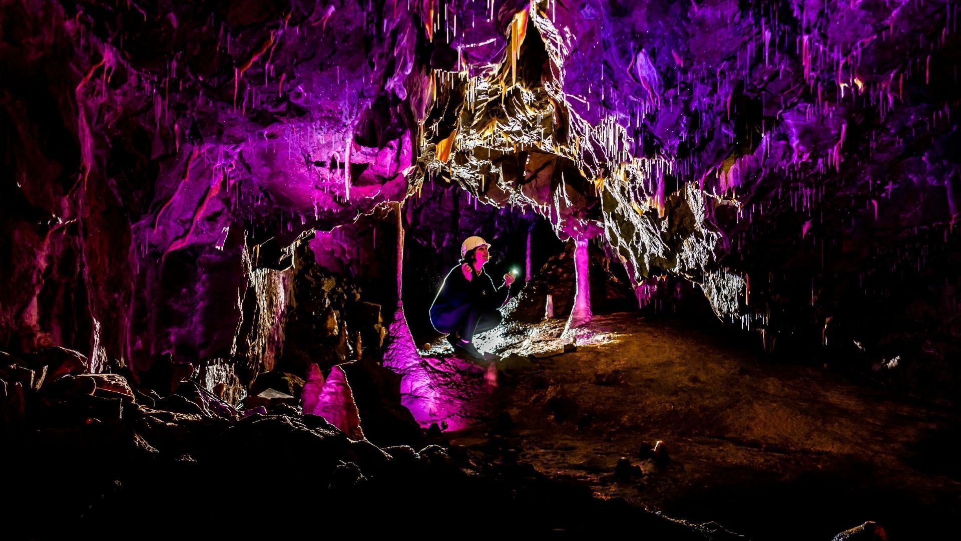 Purple-lit cave with rocky formations and a small pool or stream in the foreground