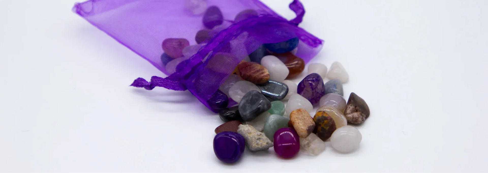 Purple drawstring bag spilling out colorful polished stones on a white surface.