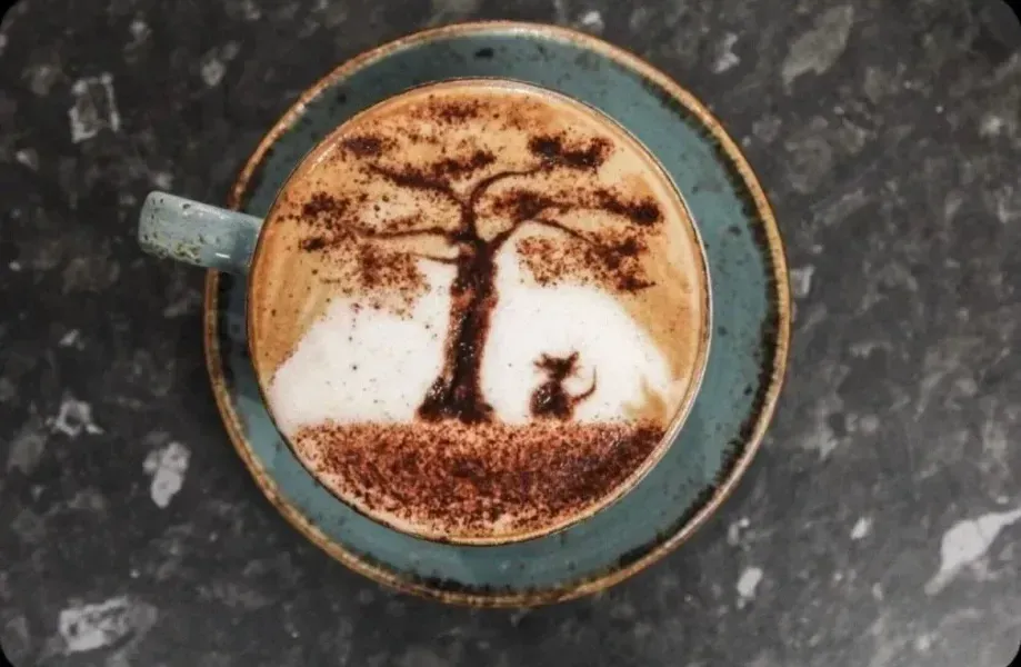 Latte with cocoa art of a tree and cat on a blue saucer.
