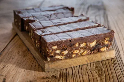Chocolate biscuit cake on a wooden board, rectangular slices with white squares on top.