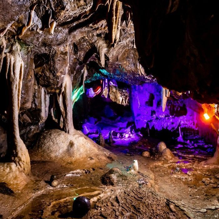 Cave interior with stalactites, stalagmites, and colorful lighting.