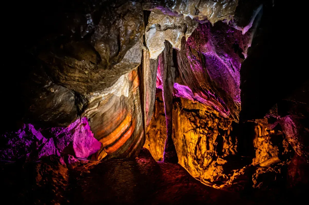 Cave interior illuminated with orange and purple lights highlighting rock formations.