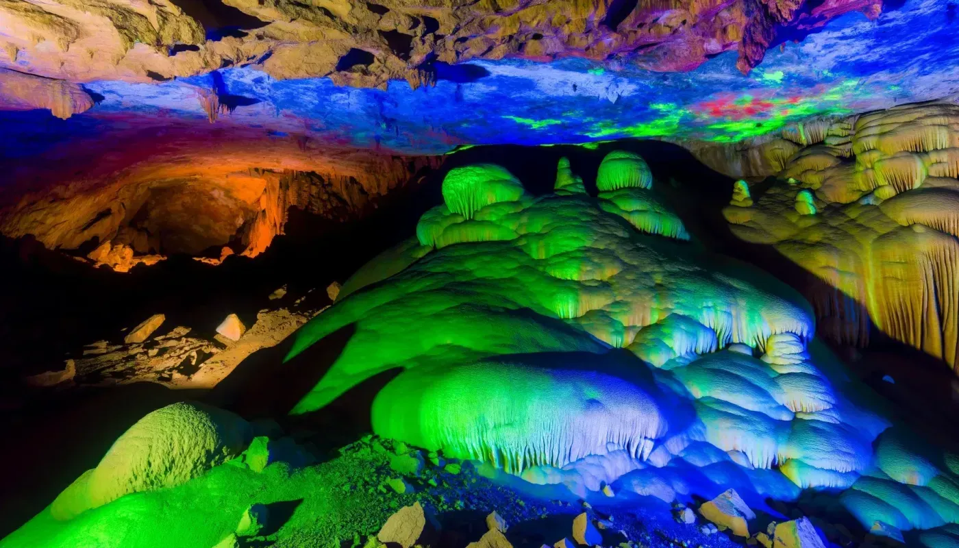 Cave interior with colorful lights illuminating formations of stalactites and stalagmites.