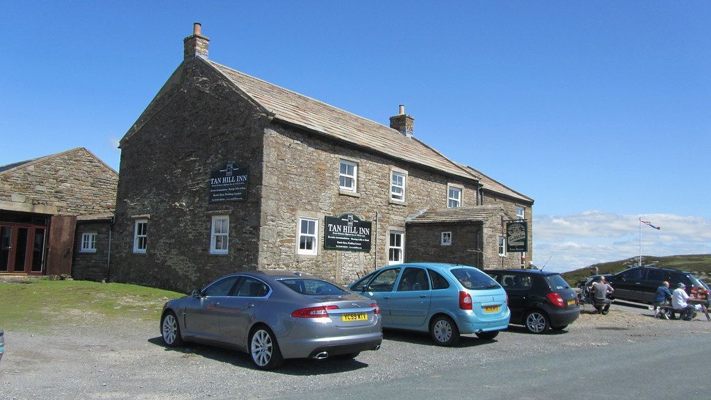 Stone building with a pub sign, cars parked in front, and a blue sky.