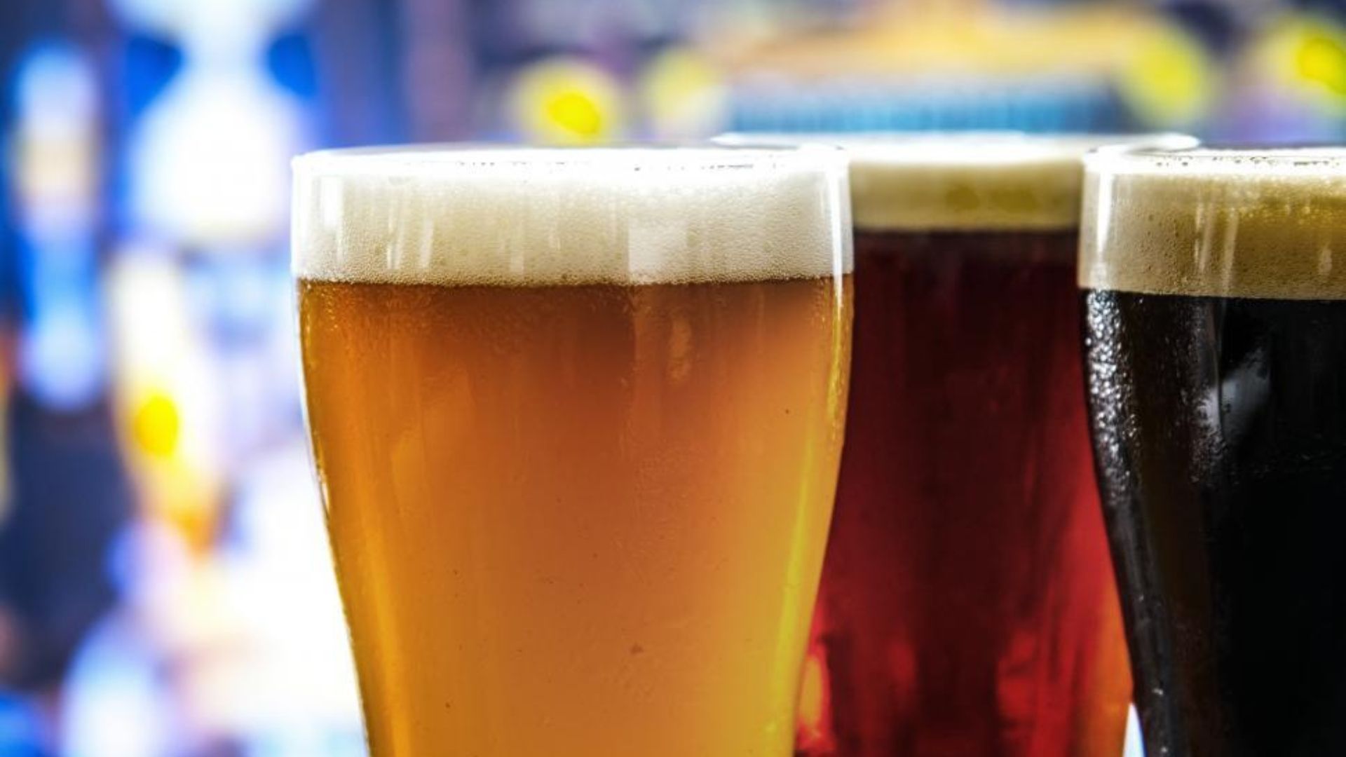 Three glasses of beer with varying colors and foam, in a bar setting.