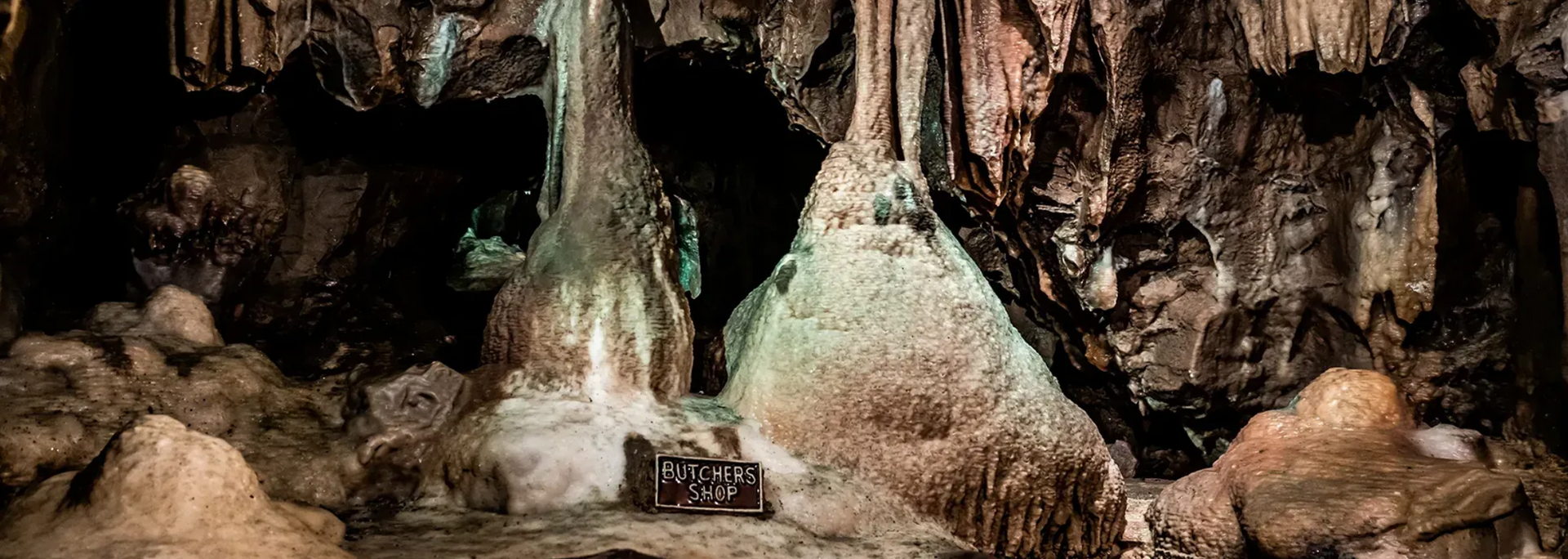 Inside a cave, formations of stalactites and stalagmites are seen.