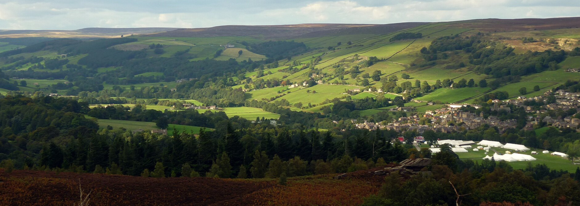 Rolling green hills and a town nestled in a valley under a cloudy sky.