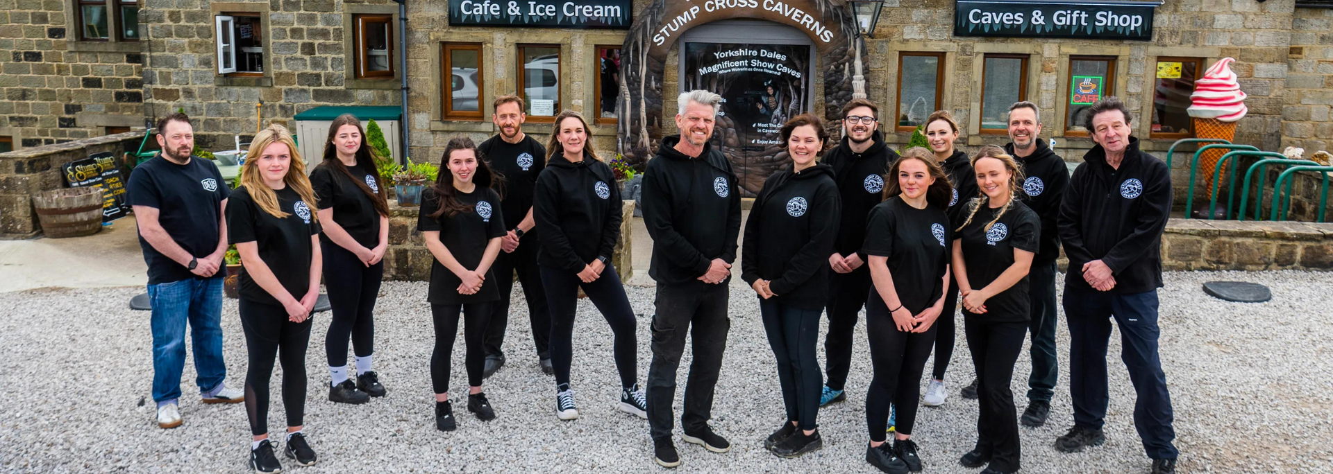 Group of people standing outside a stone building. They wear black shirts with a logo.