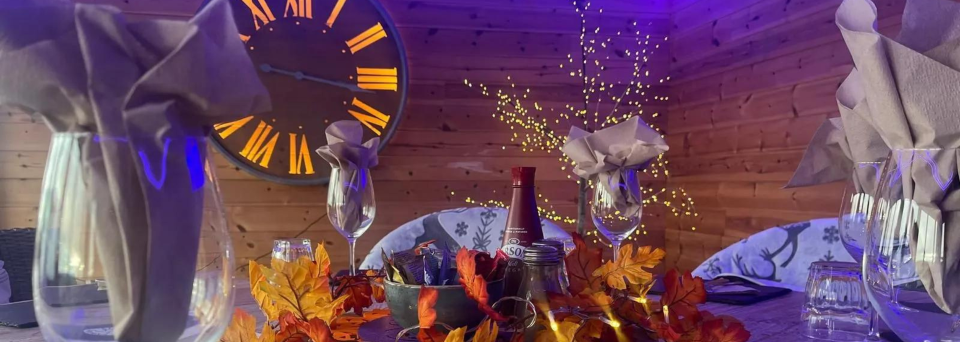 Table setting with fall foliage, wine glasses, and a clock. Purple and gold lighting.