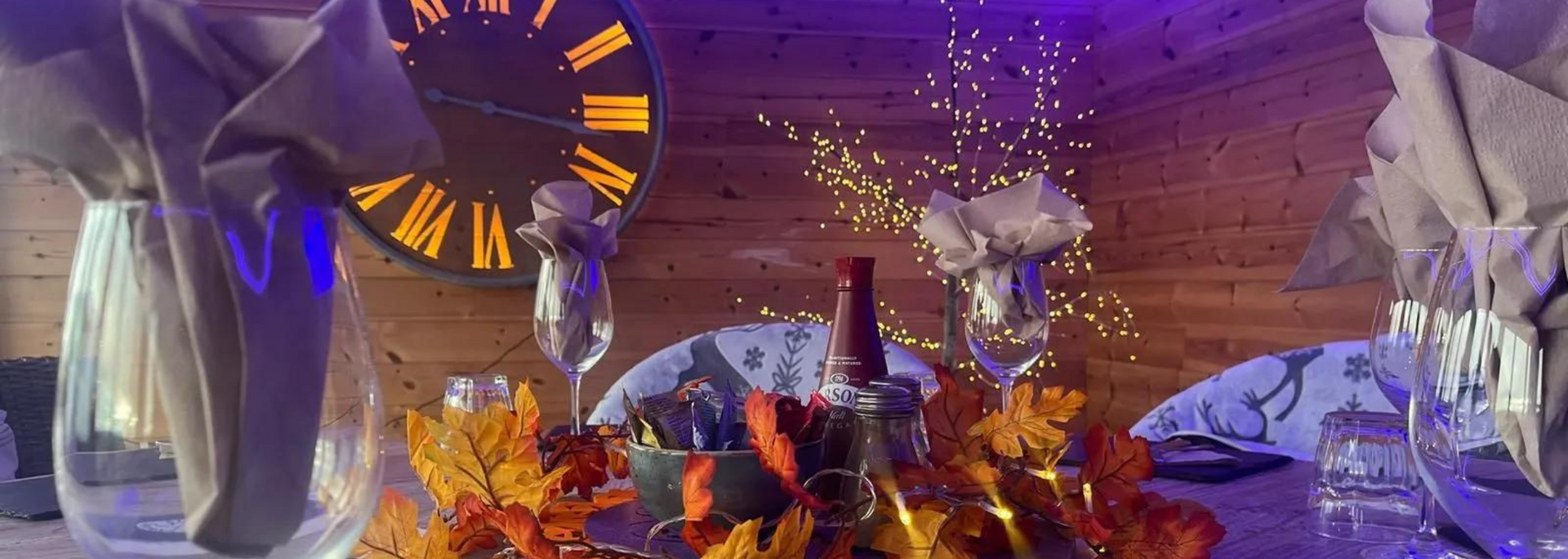 A clock, champagne glasses, and autumn decor on a table, purple lighting.