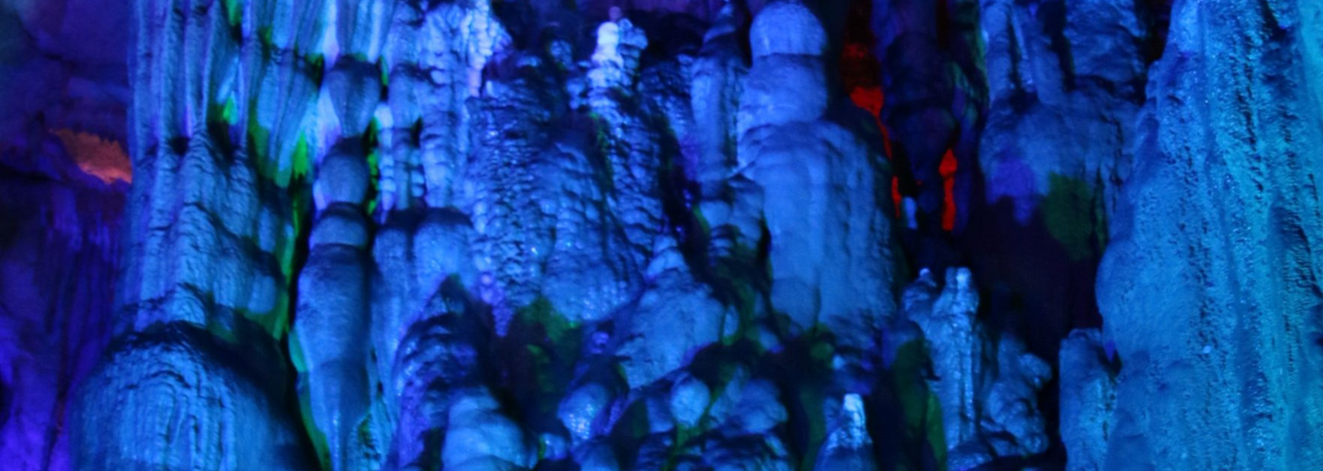 Inside a cave illuminated with blue light. Stalactites and stalagmites are visible, with green and red accents.