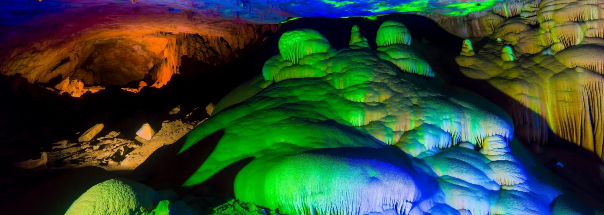 A colorful cave with green and blue formations, illuminated with colored lights.