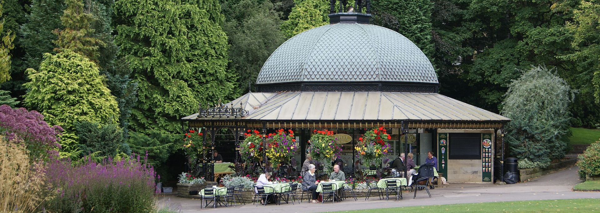 A domed building with hanging flowers, tables, and people in a park setting.