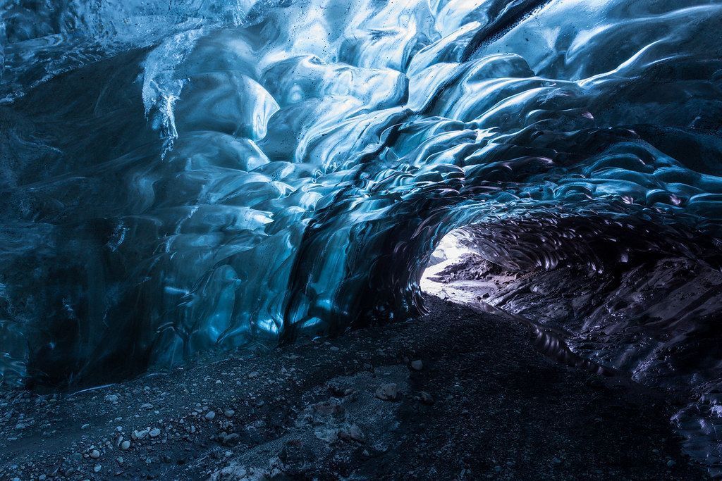 Inside a blue ice cave. Dark blue walls surround a lit opening, reflecting the light.