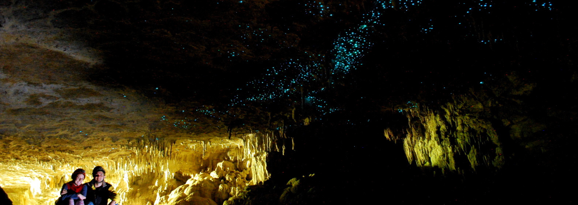 Inside a dark cave, a couple gazes up at glowing blue dots on the ceiling.