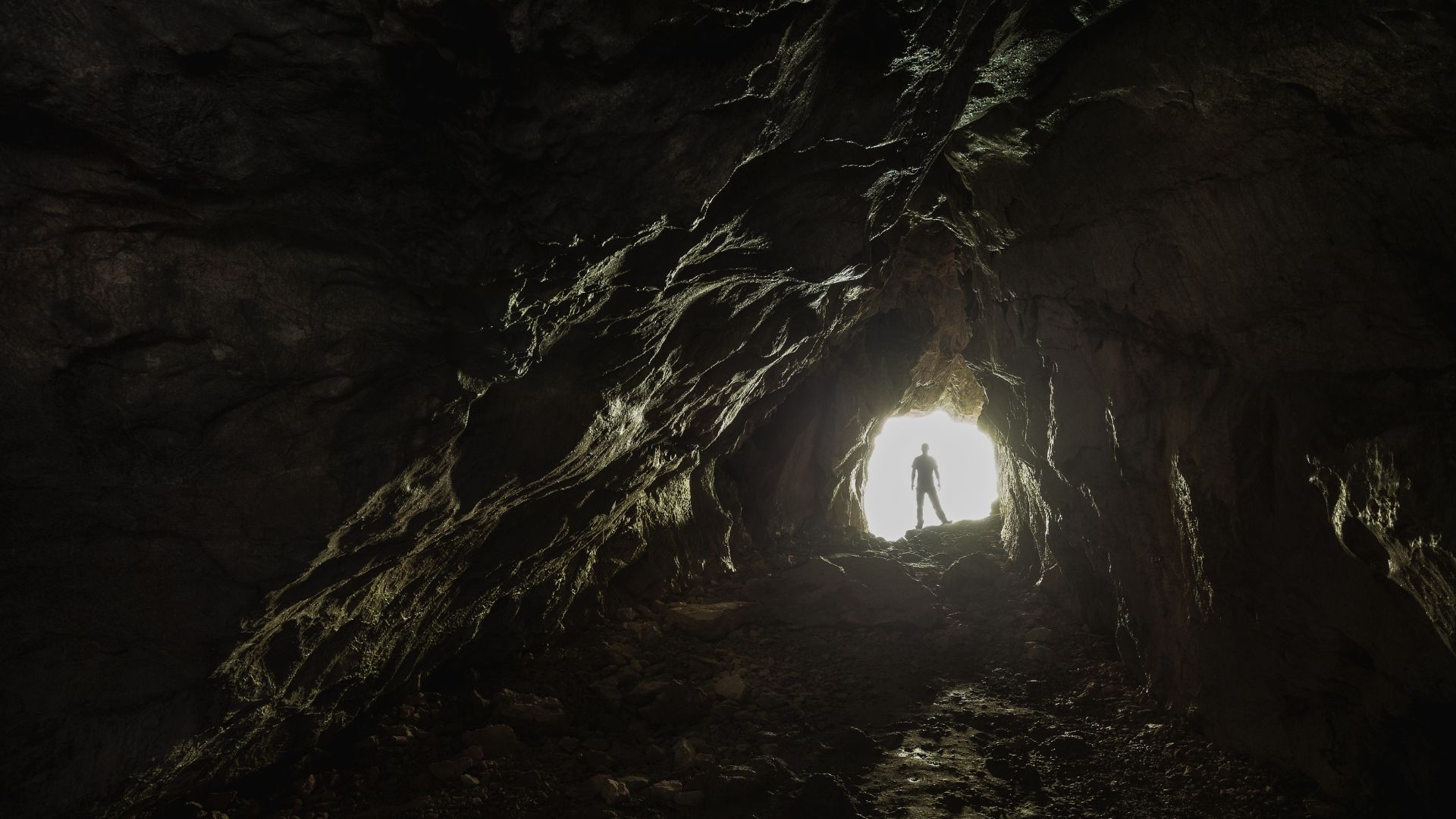 Silhouette of a person standing at a cave entrance, looking out at a bright light.