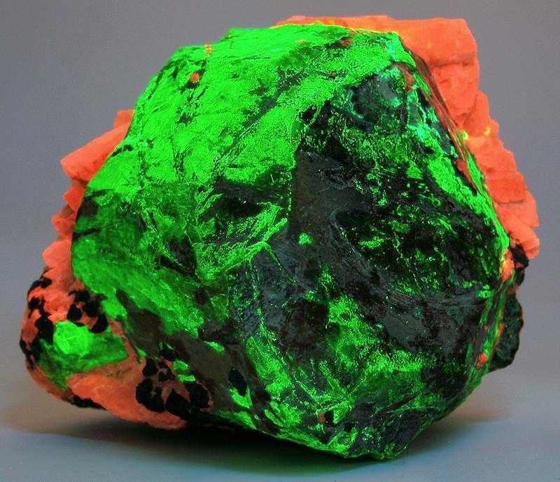 Rock formation with orange and green fluorescent minerals, with dark black patches.