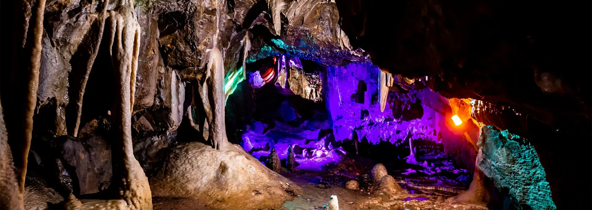 A colorful cave interior with illuminated stalactites and purple, green, and orange lighting.
