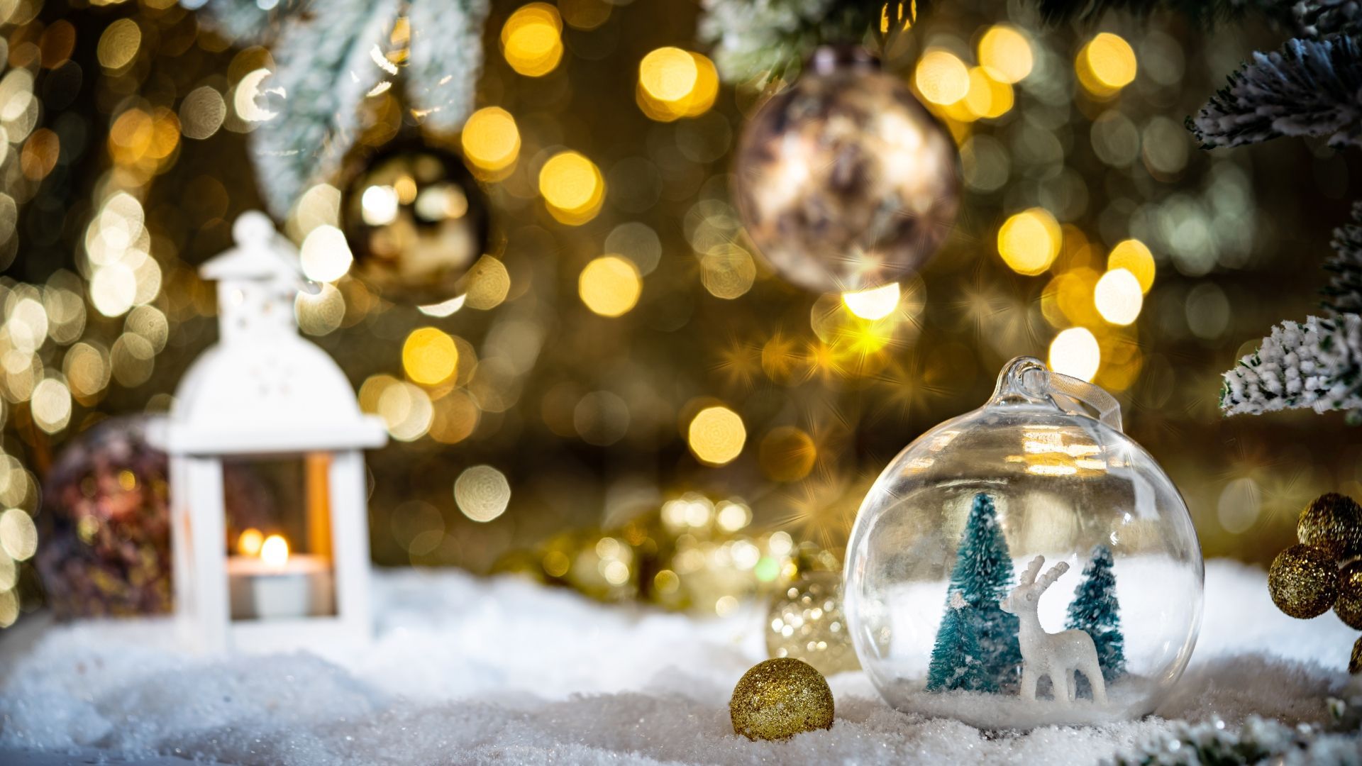 Christmas scene: snow, ornaments, lit tree, small lantern, deer inside glass ball.