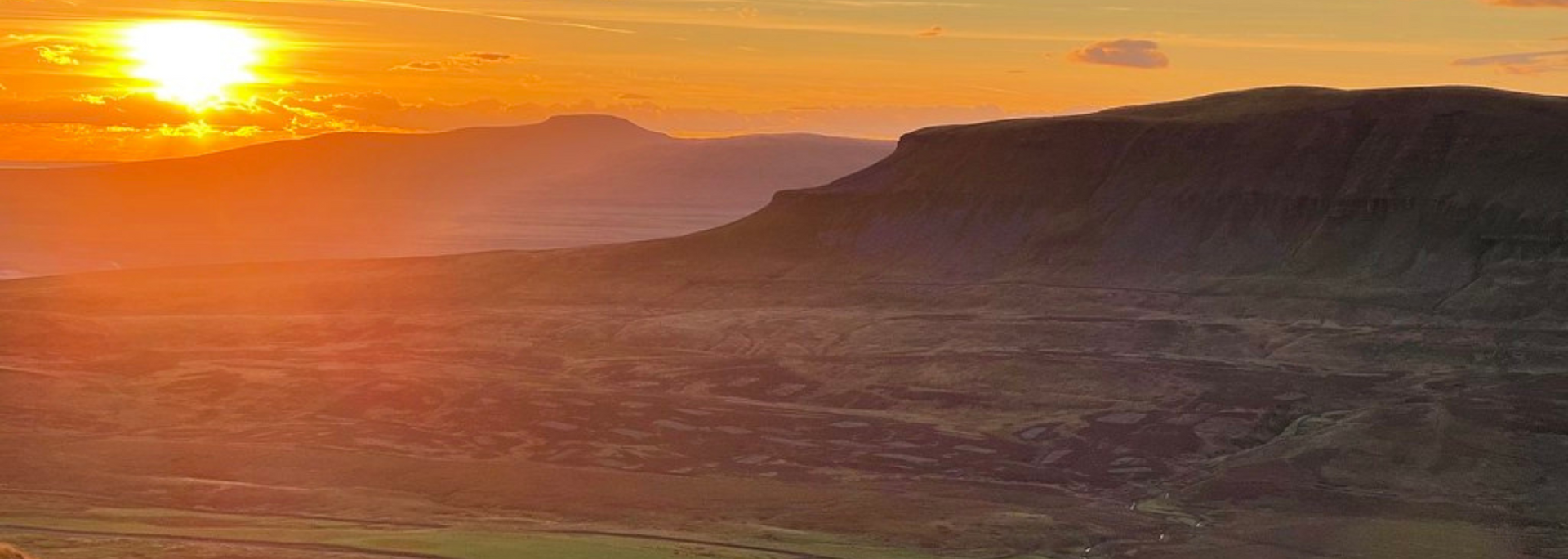 Sunset over a mountain range, bathed in orange and yellow light.