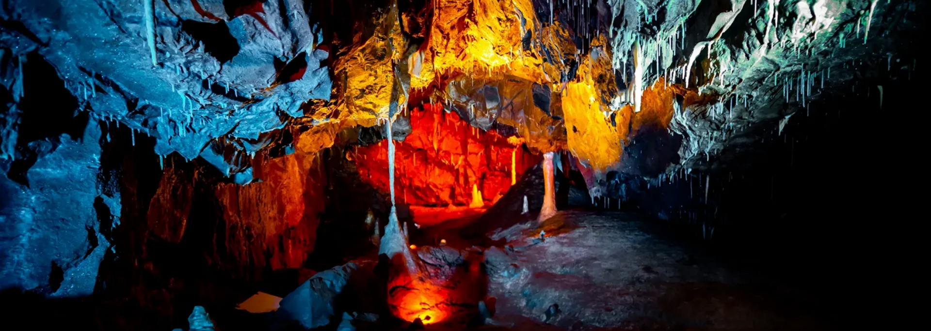 Cave interior lit with red, orange, and blue lights, showcasing stalactites and stalagmites.