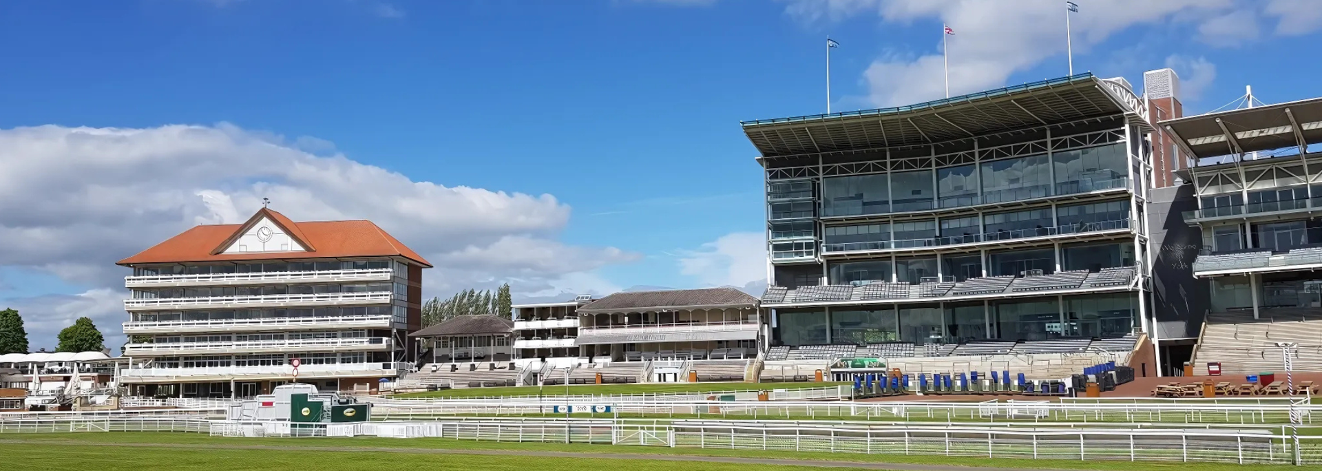 Racecourse grandstands under a blue sky, with white fences and green grass in the foreground.