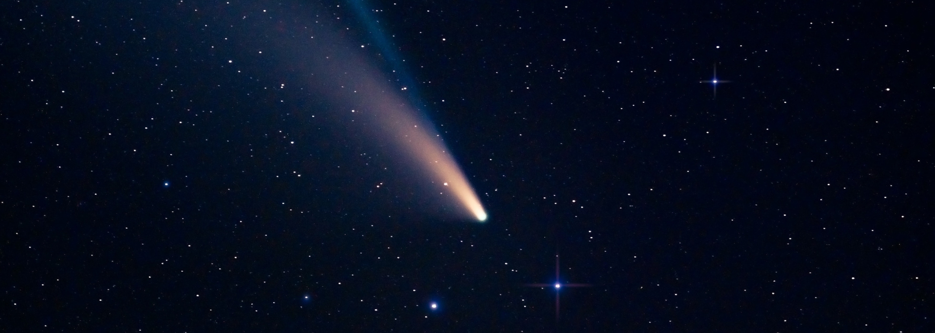A comet streaks across a dark blue starry sky.