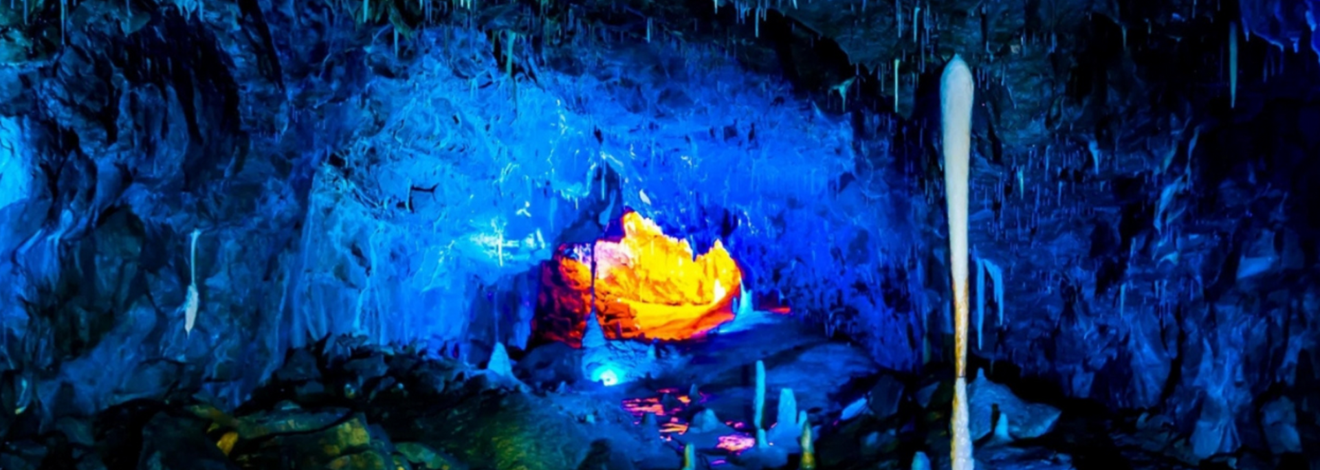 Illuminated cave interior with blue and yellow lighting, stalactites and stalagmites.