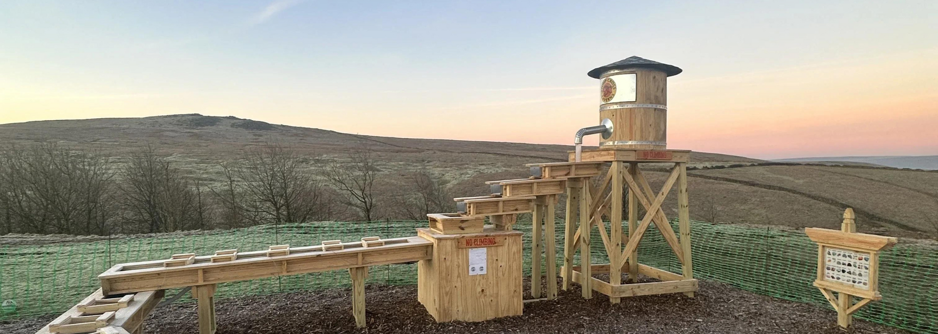 Wooden structure in a field with a lookout tower and water feature.