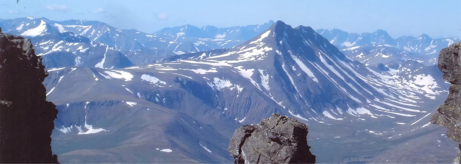 Mountain range with patches of snow under a blue sky.
