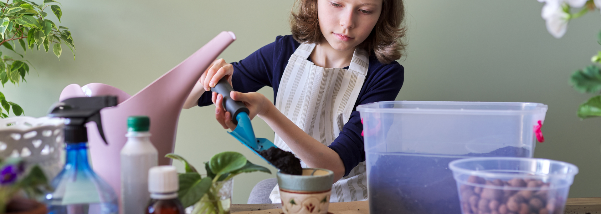 Person wearing an apron and gloves tending to plants, using a watering can.