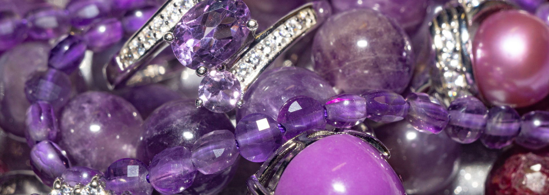 Close-up of assorted purple jewelry, including rings, beads, and a large pearl.