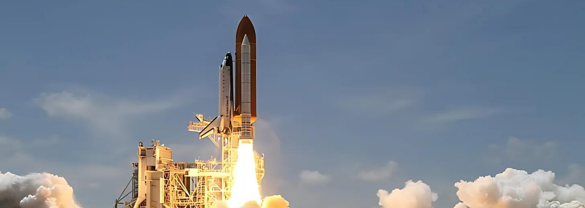 Space Shuttle lifts off from launch pad, flames erupting, cloudy blue sky.
