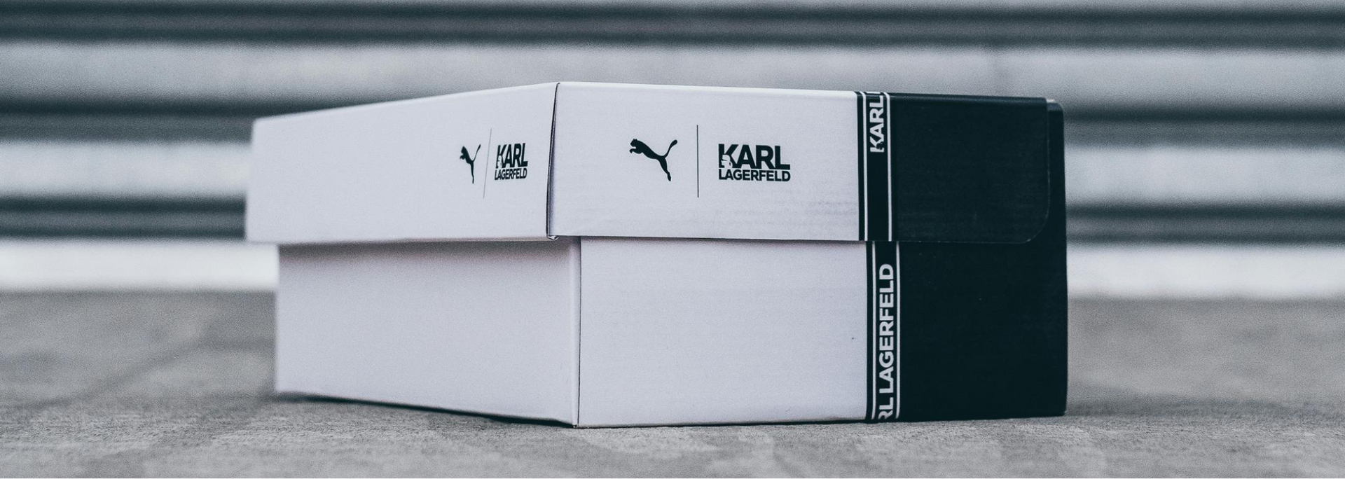 Two white Puma shoe boxes stacked, on a gray surface, with black branding.

