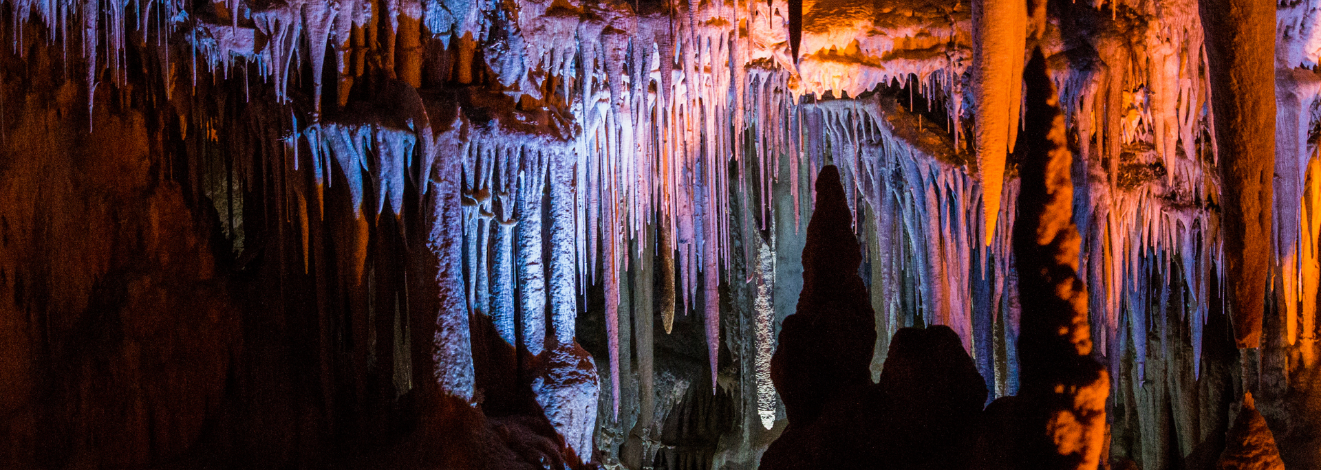 Cave interior with blue and orange lighting illuminating stalactites and stalagmites.