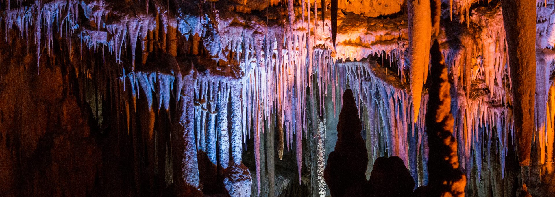 Cave interior with illuminated stalactites and stalagmites; orange and blue hues.