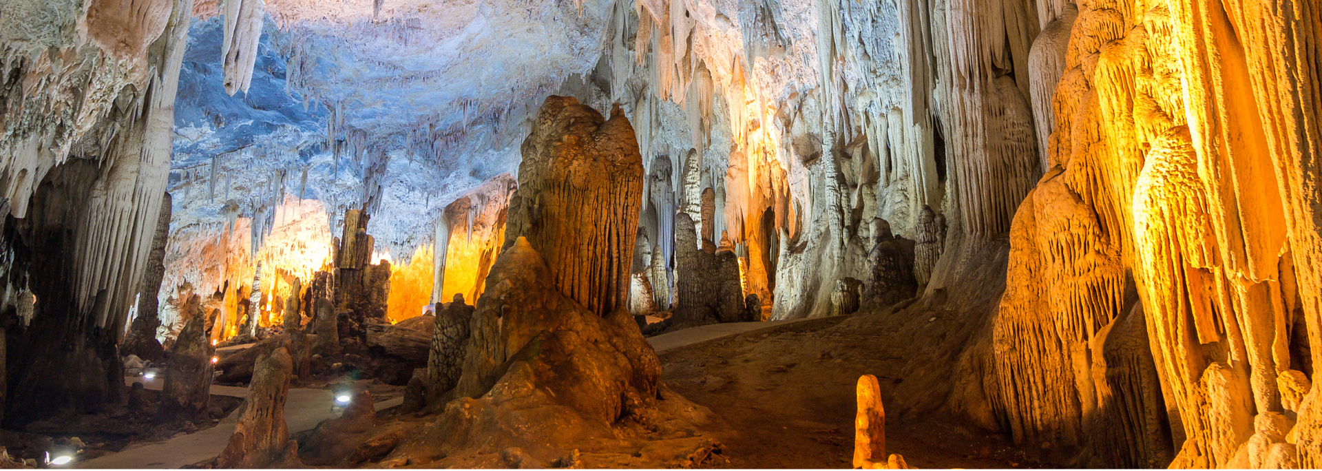 Inside a large cave lit by amber and blue light, with stalactites hanging from the ceiling.