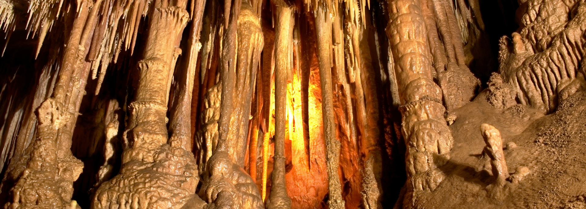 Cave formations with brown and orange hues, lit by a central light source.