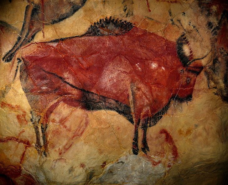 Cave painting of a bison in red and black ochre on a tan cave wall.