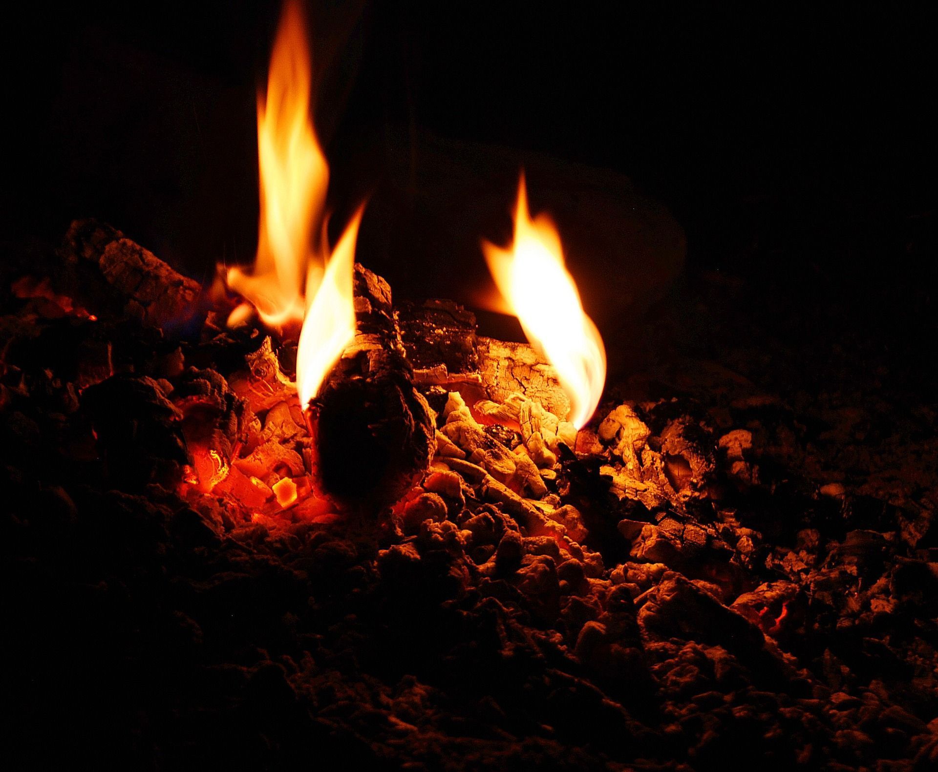 Flames rising from burning embers in darkness; orange and yellow fire, glowing red coals.