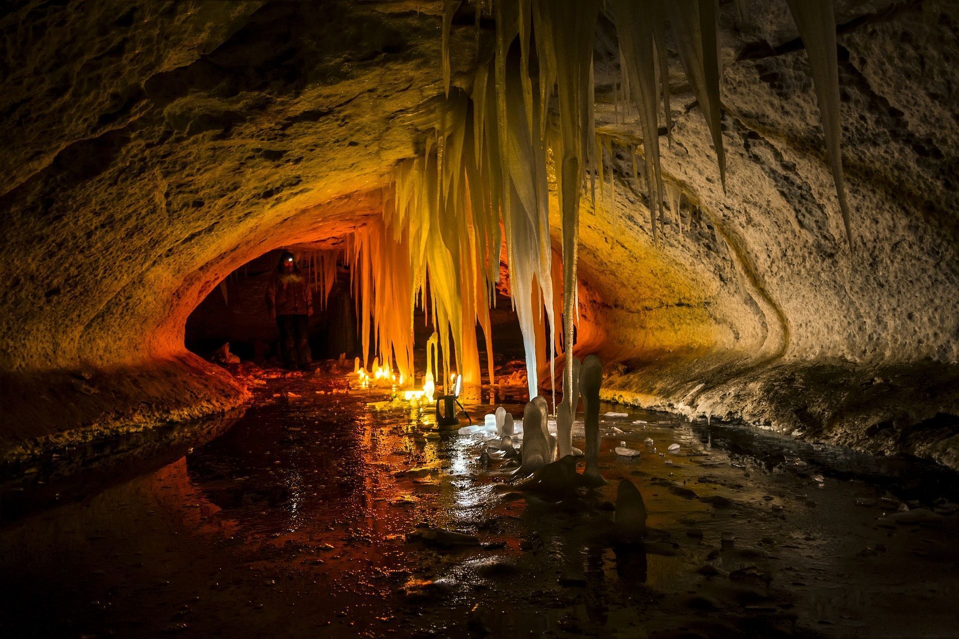 Cave interior with illuminated stalactites reflecting in the water, dark and earthy tones.