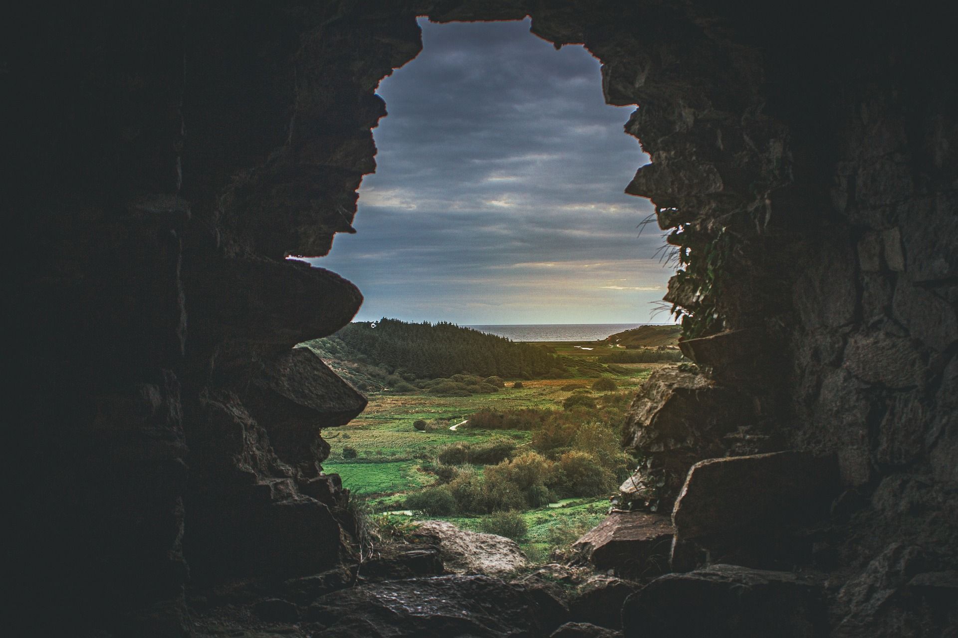 View through a stone archway, showing a green landscape and cloudy sky.
